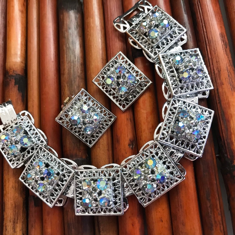 Pu&ograve; includere: Un braccialetto d'argento con un design quadrato e strass iridescenti. Il braccialetto &egrave; abbinato a orecchini coordinati.