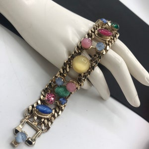 May include: A gold chain bracelet with colorful oval and round glass stones. The stones are in shades of pink, blue, green, yellow, and red.