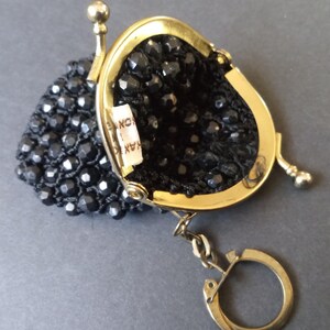 May include: A small black beaded coin purse with a gold metal frame and a gold key chain. The purse has a label that reads "HANKO INC."