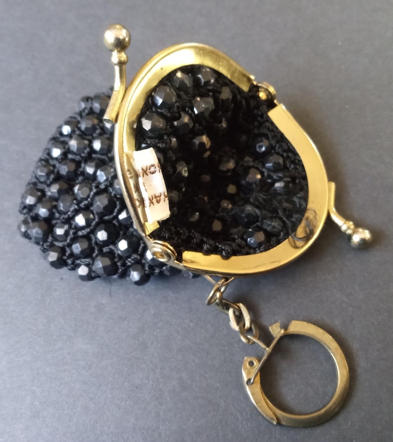 May include: A small black beaded coin purse with a gold metal frame and a gold key chain. The purse has a label that reads "HANKO INC."