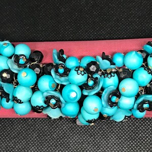 May include: A turquoise and black beaded necklace with floral accents. The beads are clustered together in a cascading design.