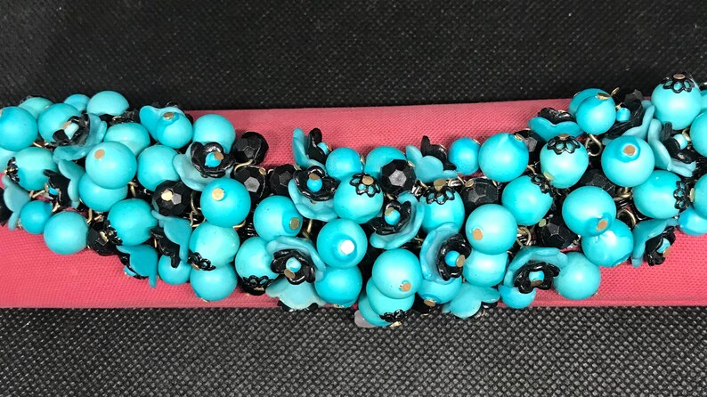 May include: A turquoise and black beaded necklace with floral accents. The beads are clustered together in a cascading design.