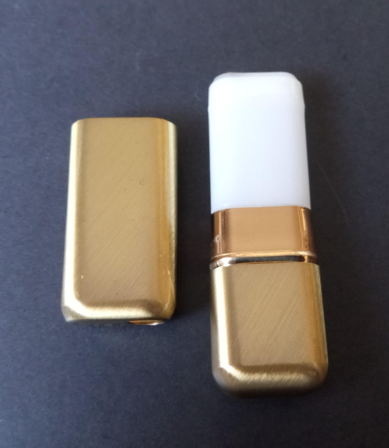 May include: Two gold-colored metal lipstick cases, one with a white top and one without. The cases have a brushed finish.