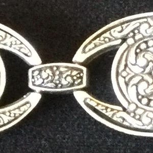 Peut inclure: Bracelet argent&eacute; au design orn&eacute;. Le bracelet pr&eacute;sente des maillons ovales avec des motifs floraux d&eacute;taill&eacute;s et des maillons rectangulaires de connexion. Un fermoir s&eacute;curise le bracelet. Le bijou est pr&eacute;sent&eacute; sur fond sombre.