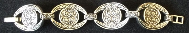 Peut inclure: Bracelet argent&eacute; au design orn&eacute;. Le bracelet pr&eacute;sente des maillons ovales avec des motifs floraux d&eacute;taill&eacute;s et des maillons rectangulaires de connexion. Un fermoir s&eacute;curise le bracelet. Le bijou est pr&eacute;sent&eacute; sur fond sombre.