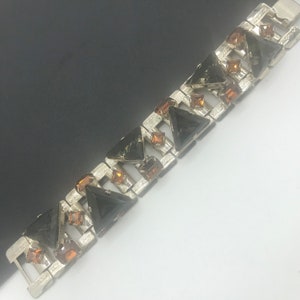 May include: A silver tone bracelet with black and amber coloured rhinestones. The bracelet is made of a series of linked squares with a triangle shaped rhinestone in each square.