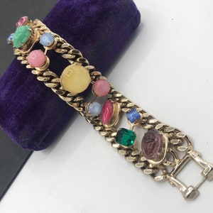 May include: A gold chain bracelet with a double row of colorful stones. The stones are in various shapes and sizes, including round, oval, and square. The stones are set in gold and are surrounded by gold chain links. The bracelet has a clasp closure.