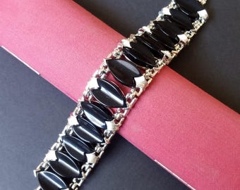 Peut inclure: Un bracelet noir et argent avec un design de chaîne et des pierres noires de forme ovale. Le bracelet est sur une surface en velours rouge.