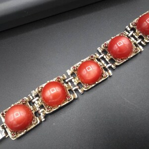 May include: A vintage bracelet featuring five large, round, coral-colored cabochons set in gold-toned metal frames. The bracelet has a silver-toned chain link design and is secured with a clasp. Small red rhinestones accent the frames.