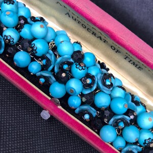 May include: A vintage turquoise and black beaded bracelet in a pink velvet box. The box has the words "Autocrat of Time" printed on it.