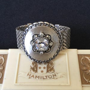 May include: A white ceramic mug with a black handle and the text "But First, Coffee" in a handwritten style. The mug is on a white surface. The mug is approximately 4 inches tall.