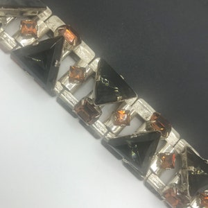 May include: A silver bracelet with a geometric design featuring alternating black and brown triangular and square rhinestones.