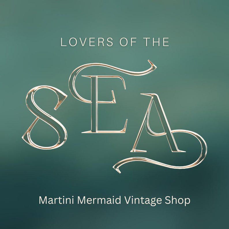 May include: A graphic design featuring the text LOVERS OF THE SEA in a metallic gold serif font with elegant flourishes, centred above the text Martini Mermaid Vintage Shop, all set against a solid, smooth, dark teal gradient background.
