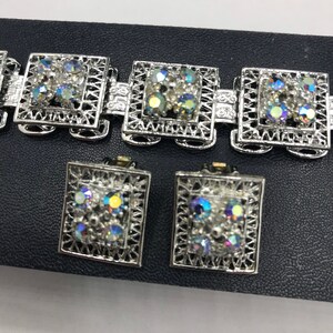 Pu&ograve; includere: Un braccialetto e un set di orecchini abbinati in tono argento con strass iridescenti. I gioielli presentano un design quadrato con un motivo a filigrana.