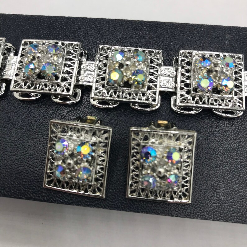 Pu&ograve; includere: Un braccialetto e un set di orecchini abbinati in tono argento con strass iridescenti. I gioielli presentano un design quadrato con un motivo a filigrana.