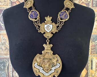 May include: A gold-toned ceremonial collar featuring a large central pendant with a goat head relief, a banner inscribed with "JUSTICE PHILANTHROPY TRUTH," and a blue enamel triangle pendant. The chain includes circular links with blue enamel details.
