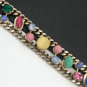 May include: A gold chain bracelet with colorful glass stones. The stones are in various shapes and sizes, including round, oval, and square. The bracelet is a statement piece and would be a great addition to any jewelry collection.