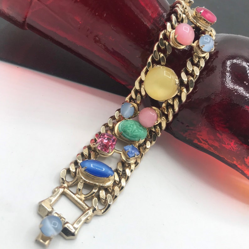 May include: A gold chain bracelet with a variety of colorful oval-shaped stones. The stones are set in gold and are arranged in a random pattern. The bracelet has a clasp closure.