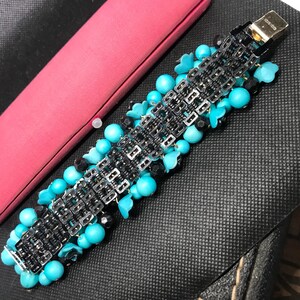 May include: A turquoise and black beaded bracelet with a metal chain link design. The bracelet is made with small turquoise and black beads, and the chain link design is made of silver metal.