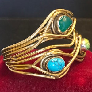 May include: A gold wire bracelet with three colorful stones. The stones are turquoise, green, and yellow.