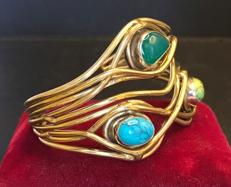 May include: A gold wire bracelet with three colorful stones. The stones are turquoise, green, and yellow.