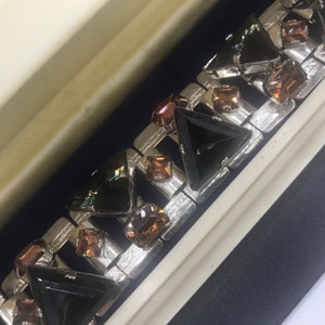 May include: A silver bracelet featuring black and brown triangular rhinestones. The bracelet is made of metal and has a geometric design.