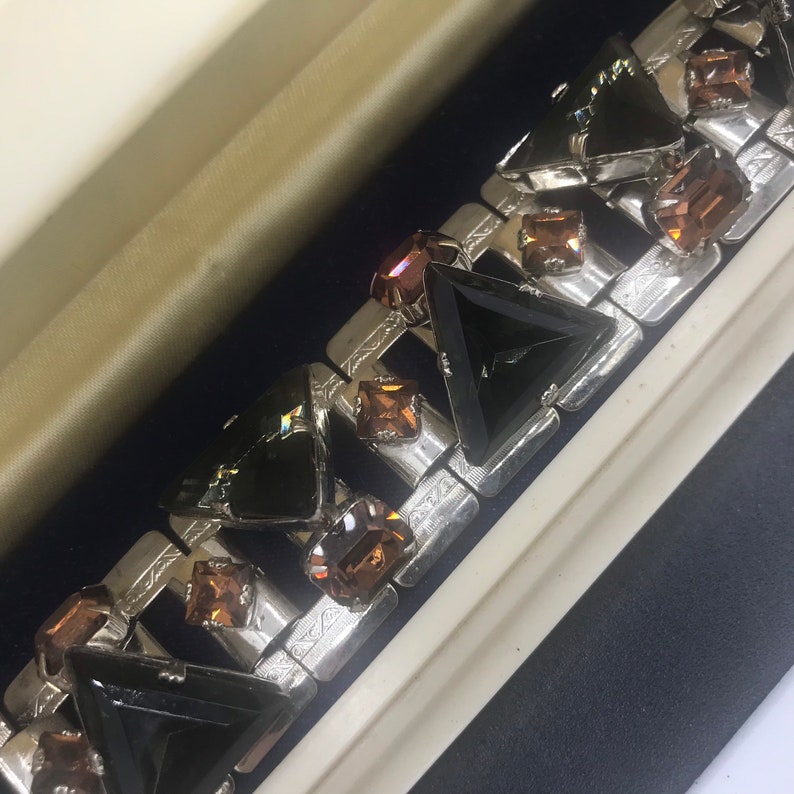 May include: A silver bracelet featuring black and brown triangular rhinestones. The bracelet is made of metal and has a geometric design.
