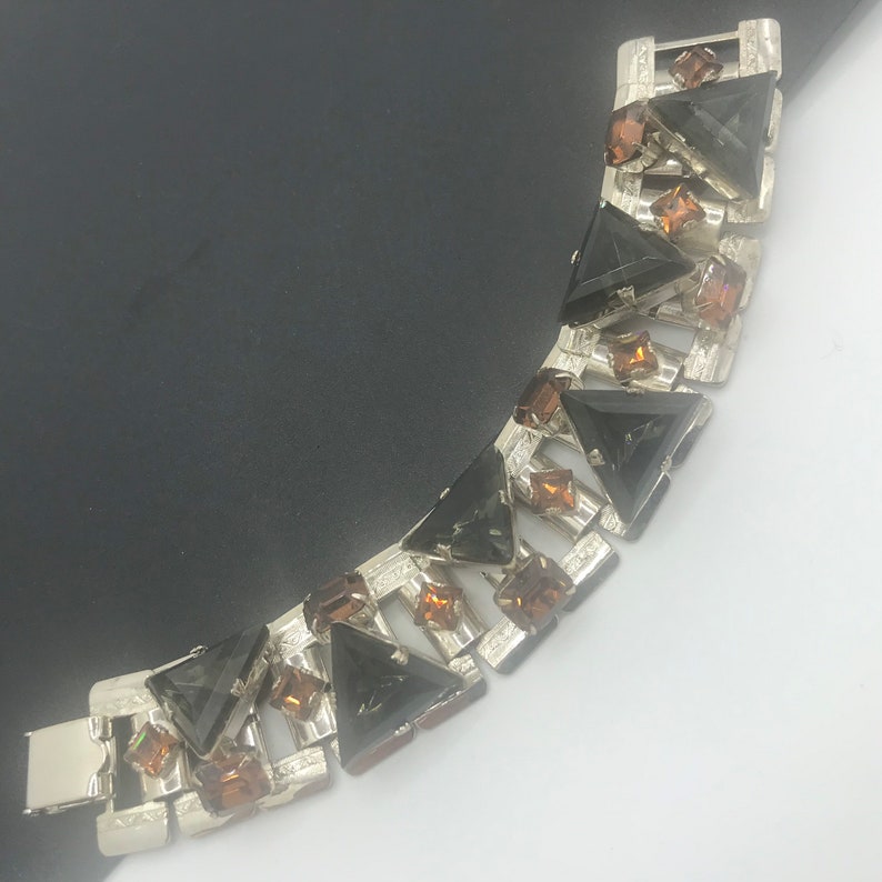 May include: A silver tone bracelet with a geometric design featuring black and brown triangular rhinestones.