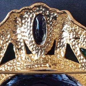 Peut inclure: Broche dor&eacute;e avec un motif en &eacute;mail noir et vert. La broche pr&eacute;sente une grande pierre ovale au centre et des pierres plus petites autour des bords. Le dos de la broche a une &eacute;pingle et une signature qui lit "Chanel."