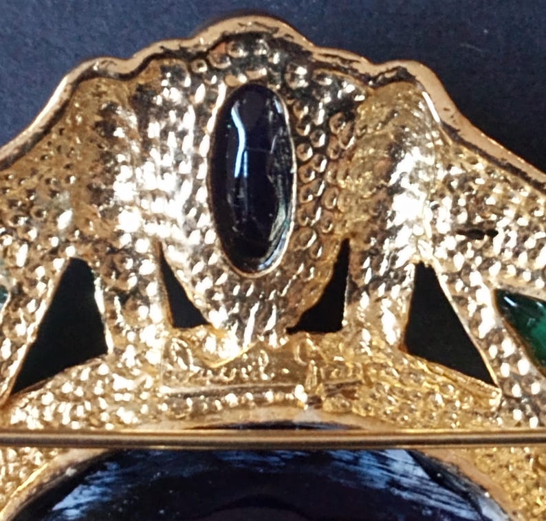 Peut inclure: Broche dor&eacute;e avec un motif en &eacute;mail noir et vert. La broche pr&eacute;sente une grande pierre ovale au centre et des pierres plus petites autour des bords. Le dos de la broche a une &eacute;pingle et une signature qui lit "Chanel."
