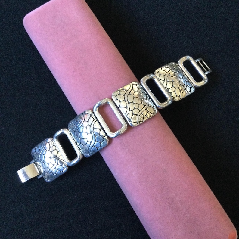May include: A silver-toned link bracelet featuring alternating rectangular segments. Three segments have a textured, pebble-like pattern, while the connecting links are smooth, open, and rectangular. The bracelet includes a metal clasp closure.