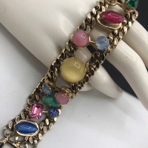 May include: A gold chain bracelet with colorful oval and rectangular shaped stones. The stones are in shades of pink, blue, green, yellow, and red.