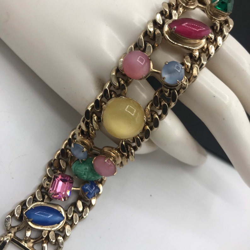 May include: A gold chain bracelet with colorful oval and rectangular shaped stones. The stones are in shades of pink, blue, green, yellow, and red.