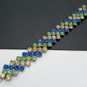 May include: A silver bracelet with blue, green, and yellow rhinestones arranged in a chevron pattern.