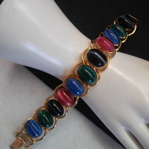 May include: A gold chain bracelet with oval-shaped, multi-colored stones. The stones are blue, green, black, and red.