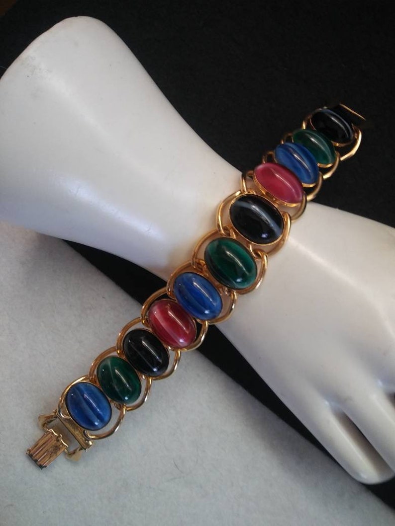 May include: A gold chain bracelet with oval-shaped, multi-colored stones. The stones are blue, green, black, and red.