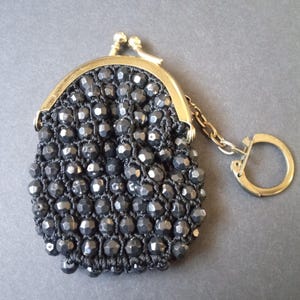 May include: A small black beaded coin purse with a gold metal clasp and a gold chain with a key ring.