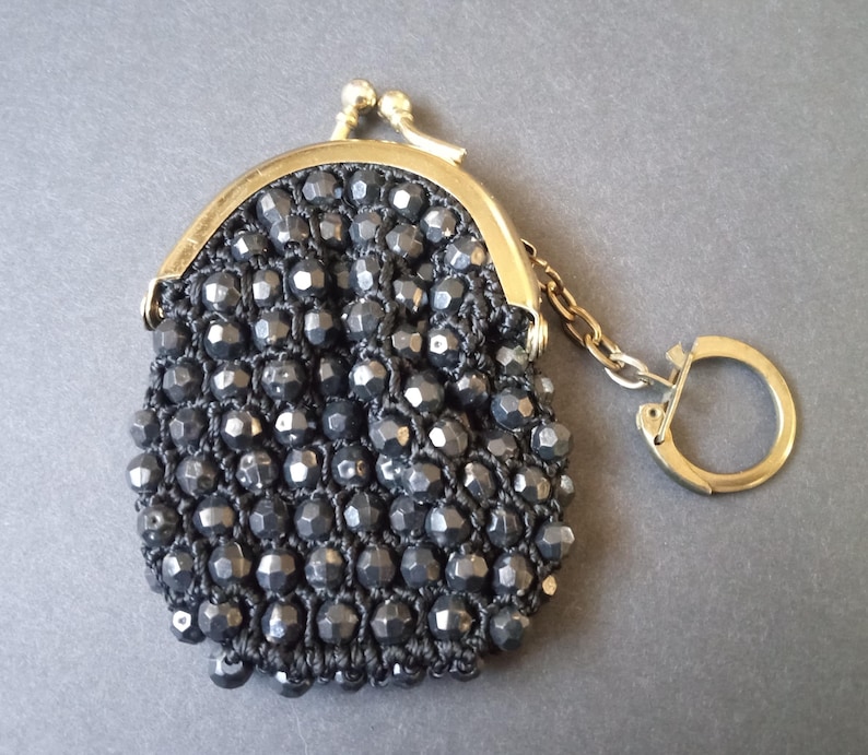 May include: A small black beaded coin purse with a gold metal clasp and a gold chain with a key ring.