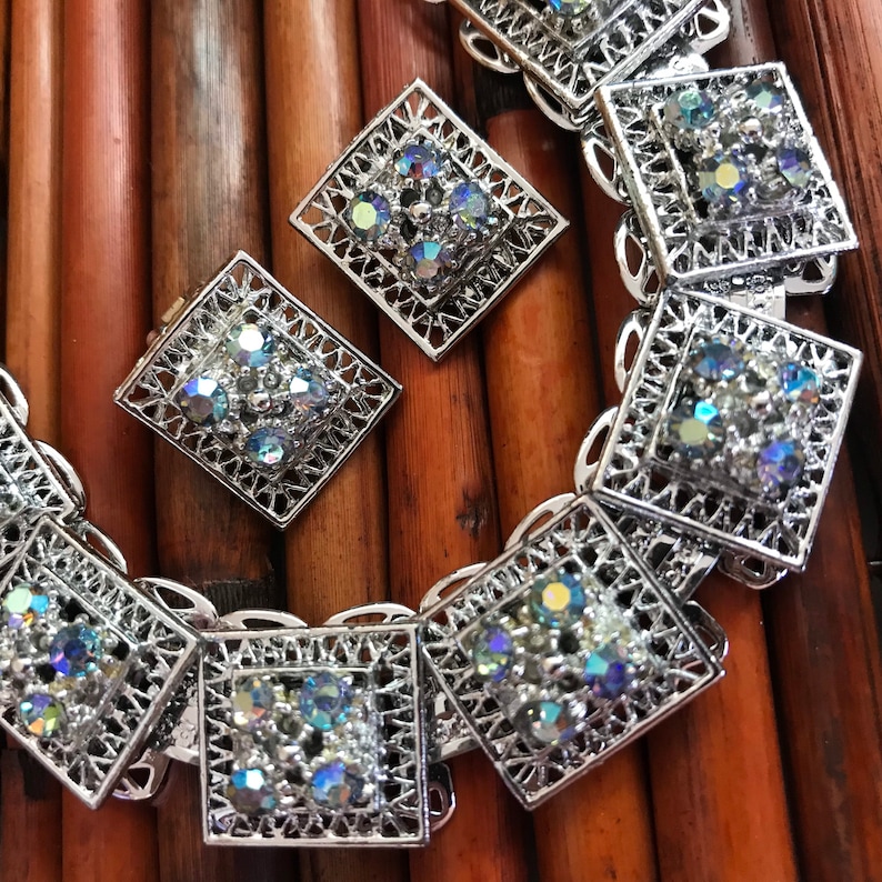 Pu&ograve; includere: Una collana d'argento con un motivo ripetitivo di ciondoli quadrati. Ogni ciondolo &egrave; decorato con strass iridescenti.