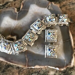 Pu&ograve; includere: Un set di braccialetto e orecchini in argento con maglie quadrate e strass iridescenti.