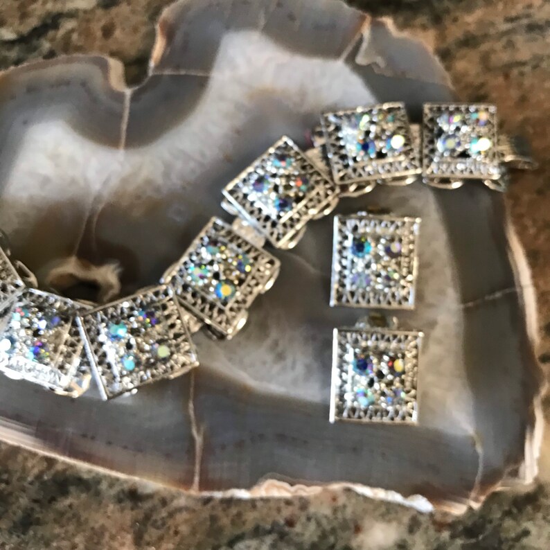 Pu&ograve; includere: Un set di braccialetto e orecchini in argento con maglie quadrate e strass iridescenti.