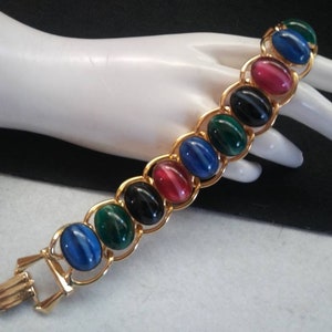 May include: A gold chain bracelet with oval-shaped, multi-colored stones. The stones are red, green, blue, and black.