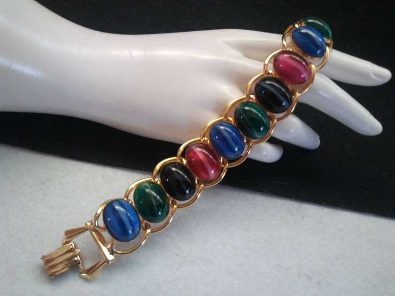 May include: A gold chain bracelet with oval-shaped, multi-colored stones. The stones are red, green, blue, and black.