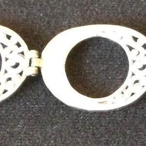 Może przedstawiać: Srebrna bransoletka z pięcioma owalnymi ogniwami z ażurowymi wzorami. Bransoletka, z zapięciem, jest prezentowana na ciemnym tle. Biżuteria odpowiednia do noszenia na co dzień lub na specjalne okazje.