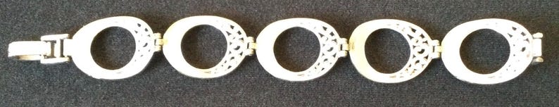 Może przedstawiać: Srebrna bransoletka z pięcioma owalnymi ogniwami z ażurowymi wzorami. Bransoletka, z zapięciem, jest prezentowana na ciemnym tle. Biżuteria odpowiednia do noszenia na co dzień lub na specjalne okazje.