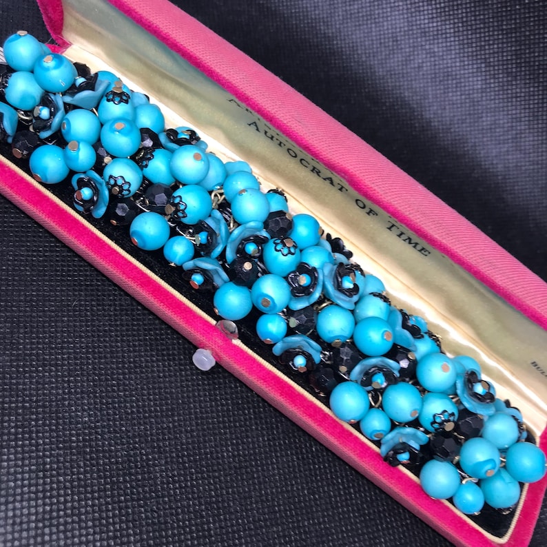 May include: A turquoise and black beaded bracelet in a pink velvet box with the words "Autocrat of Time" on the lid.
