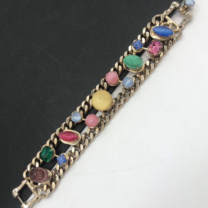 May include: A gold chain bracelet with colorful oval-shaped stones. The stones are in shades of pink, blue, green, and yellow.