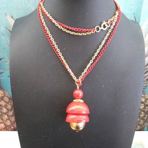 May include: A layered necklace with a red and gold pendant. The pendant is made of three stacked red circles with a gold ball at the bottom.