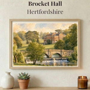 May include: A framed landscape painting titled Brocket Hall Hertfordshire depicting a large brick manor house situated behind a stone arched bridge over a waterfall. The scene includes lush green trees, a grassy landscape, and a blue sky.
