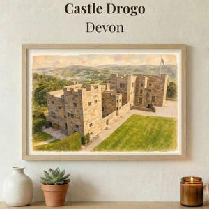 May include: A framed watercolor print titled Castle Drogo Devon, depicting a stone castle with multiple towers and battlements set against a landscape of rolling green hills under a soft sky, with a green lawn in the foreground.